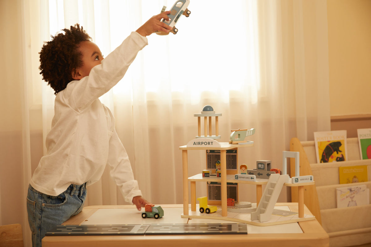 Child playing with toy cars and a toy airport set in a room with curtains.